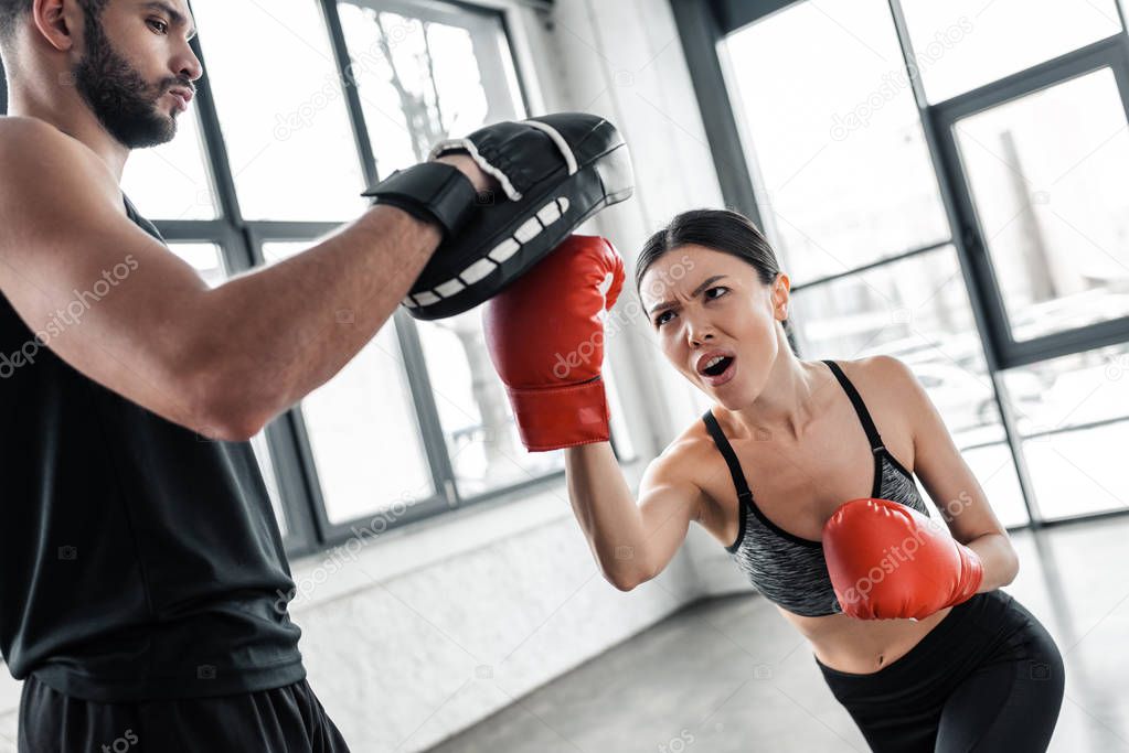 aggressive young sportswoman boxing and exercising with male trainer in gym