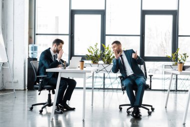 businessmen in formal wear gossiping while sitting in modern office  clipart
