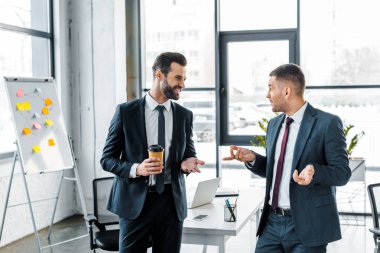 Kağıt bardak tutan ve modern ofis iş arkadaşı ile konuşurken yakışıklı işadamı 