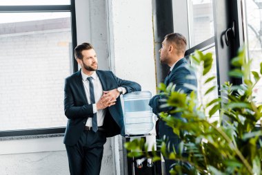 businessman in formal wear talking with coworker in modern office  clipart