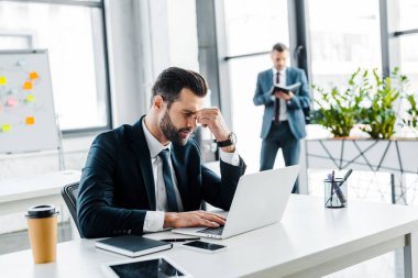 selective focus of tired businessman holding head in modern office  clipart