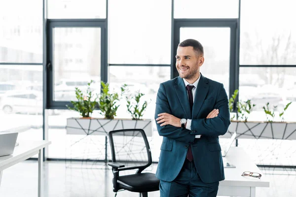 近代的なオフィスに組んだ腕の側に立って朗らかビジネスマン — ストック写真