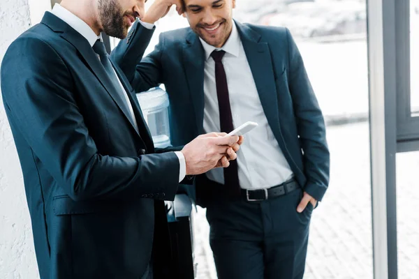 stock image businessman looking at smartphone near colleague standing with hand in pocket