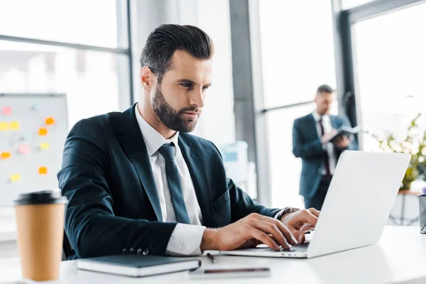 Homem Negócios Focado Digitando Laptop Com Colega Trabalho Segundo Plano — Fotografia de Stock