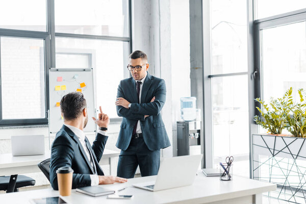 selective focus of handsome businessman in glasses looking at coworker showing middle finger 