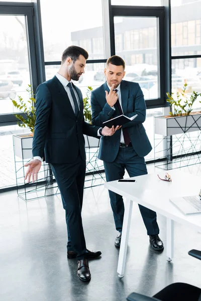 Bonito Empresário Segurando Notebook Enquanto Conversa Com Colega Escritório Moderno — Fotografia de Stock