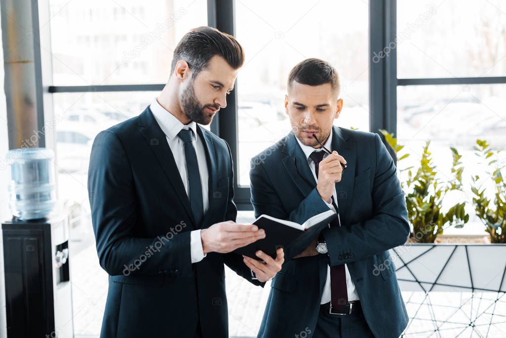 handsome businessman holding notebook near colleague in modern office 