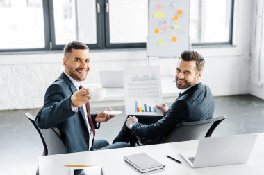seçici odak kağıt Kupası ile mutlu iş arkadaşınız yakınındaki grafikleriyle holding neşeli işadamı 