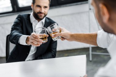 selective focus of businessman toasting glasses of whiskey with coworker  clipart
