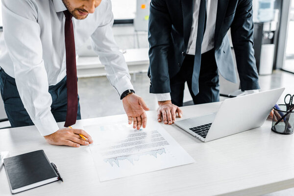 обрезанный вид бизнесменов, смотрящих на документ с диаграммой на столе
 