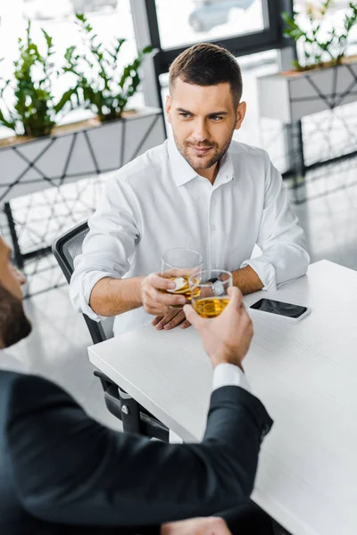 英俊的商人敬酒与威士忌 而坐在现代办公室与同事 — 图库照片