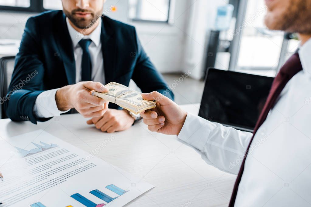 selective focus of businessman giving dollar banknotes to colleague in modern office 