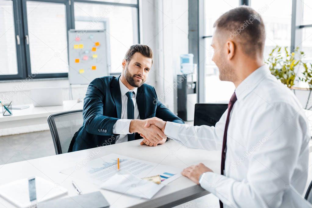 selective focus of businessman shaking hands with coworker in modern office 