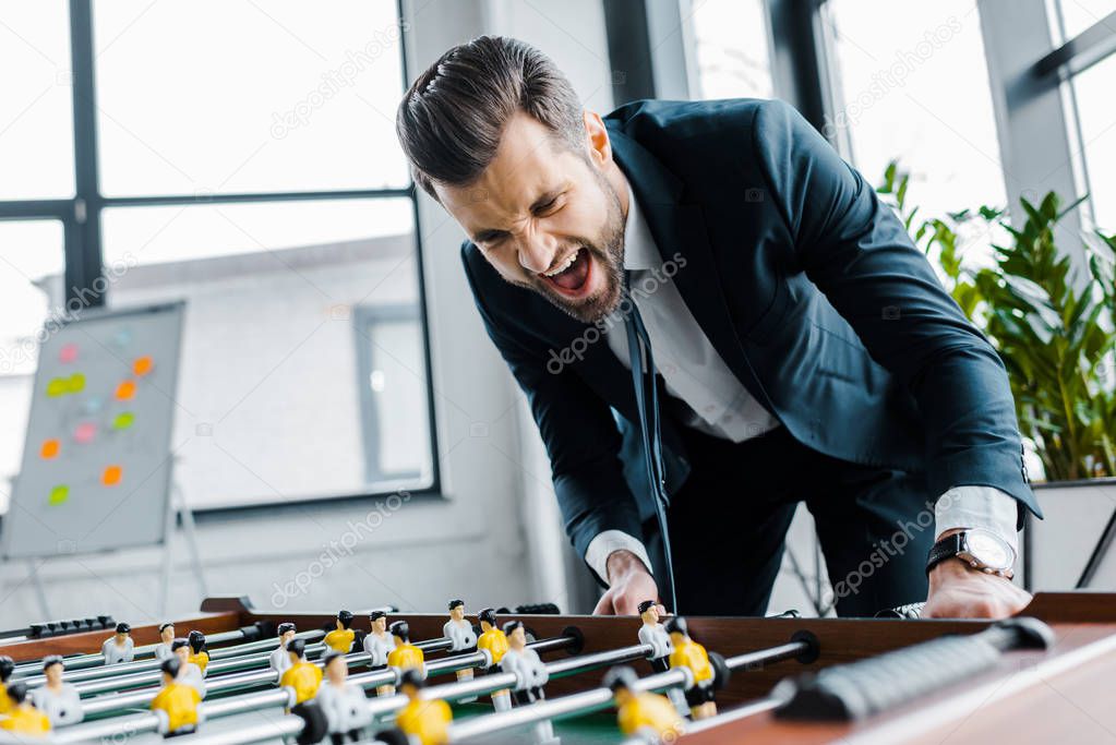 cheerful bearded businessman in formal wear playing table football 