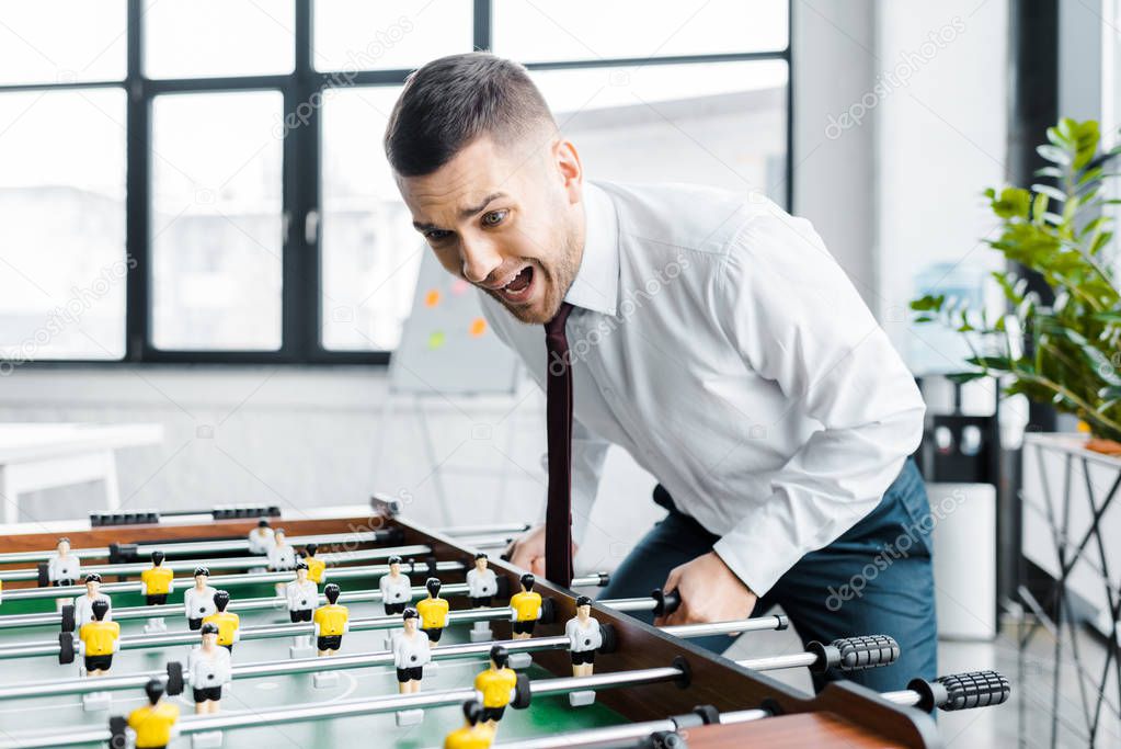 excited businessman in formal wear screaming while  playing table football 