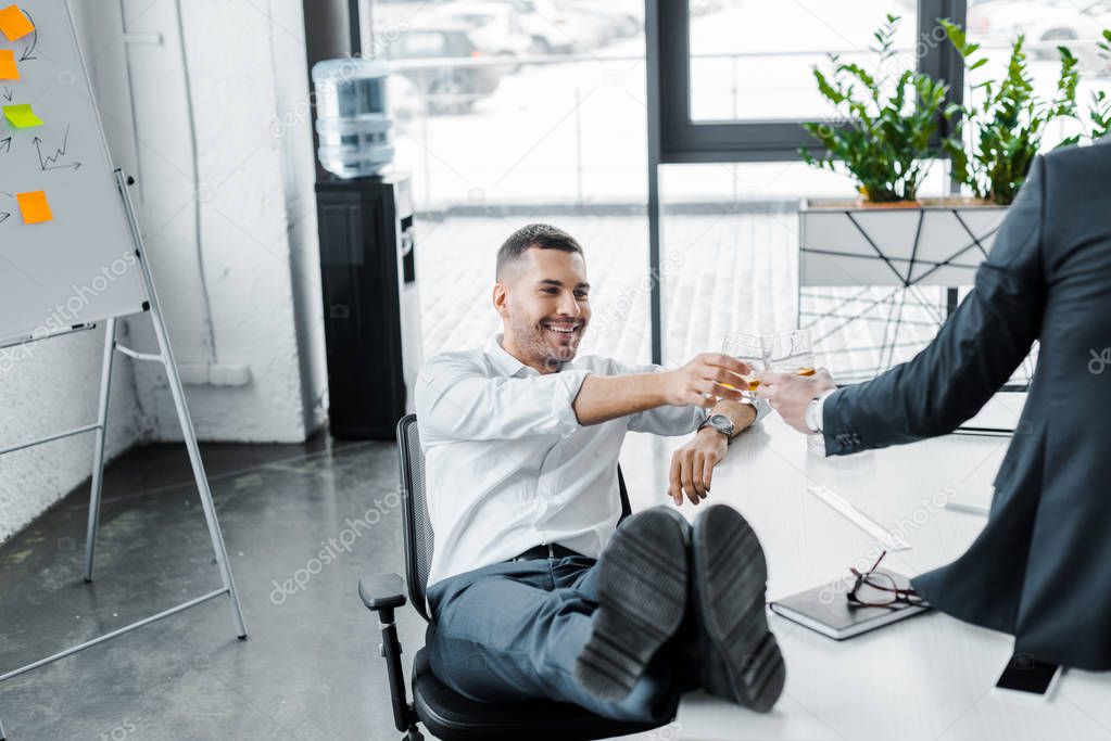 smiling businessman clinking with alcohol drink in glass with coworker in modern office 