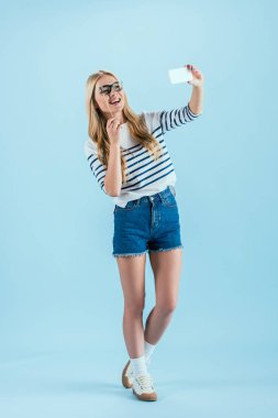 Tam boy görünüm gülen kadının selfie oyuncak gözlüklü üzerinde mavi arka plan yapma