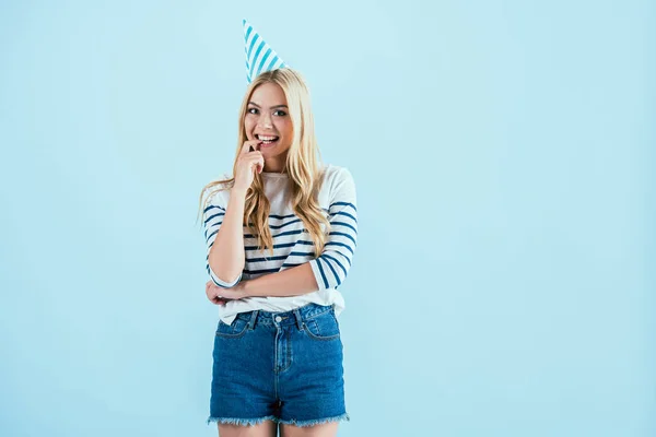 Girl in party hat biting finger isolated on blue