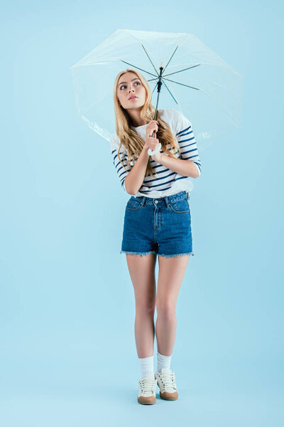 Woman in casual outfit holding umbrella on blue background