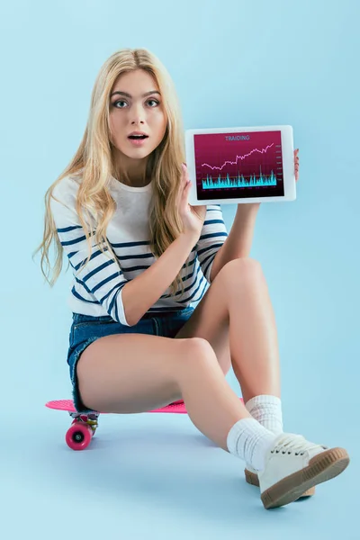 美丽的惊喜女孩摆在长板上 并显示数字平板电脑与在蓝色背景的横穿应用程序 — 图库照片