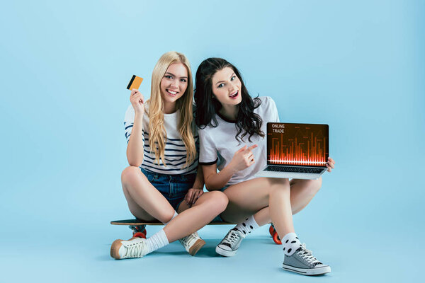 Блаженные друзья на Лонгборде держат кредитную карту и ноутбук с интернет-сайта торговли на синем фоне

