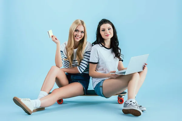 漂亮的女孩与笔记本电脑和信用卡坐在蓝色背景的长板上 — 图库照片