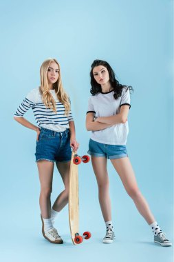 Şirin kızlar longboard üzerinde mavi arka plan ile poz
