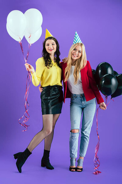 Studio shot of smiling girls with balloons embracing on purple background