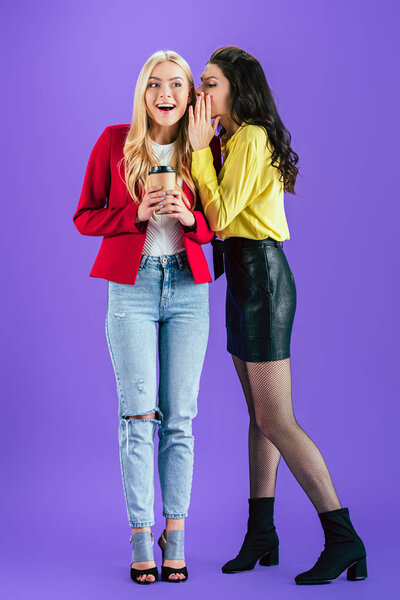 Brunette girl whispering gossips to friend on purple background