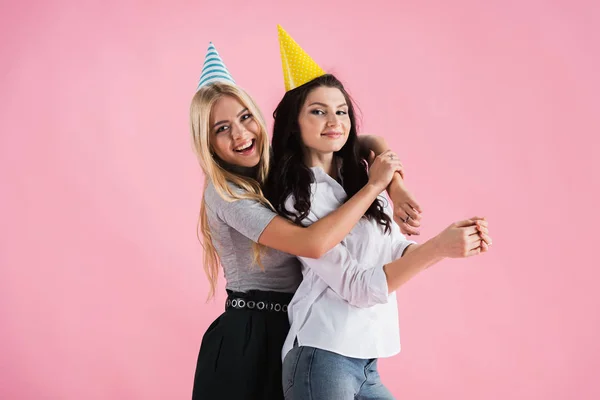 Chicas Alegres Sombreros Fiesta Abrazando Con Sonrisa Aislada Rosa — Foto de Stock