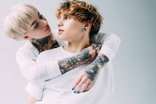 blonde girl with tattoos looking at boyfriend with curly hair isolated on grey