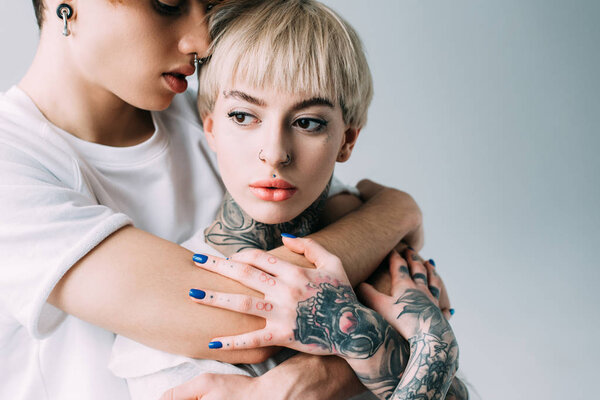  handsome boyfriend embracing blonde woman with tattoos isolated on grey