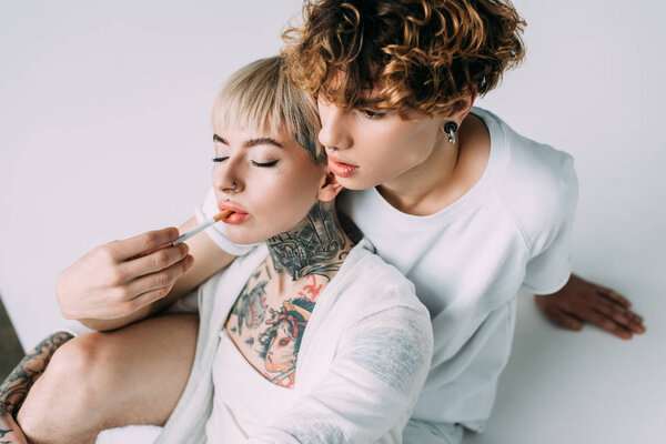 handsome man with curly hair putting cigarette in mouth of blonde tattooed girl isolated on grey