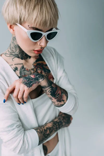 attractive woman with tattoos wearing sunglasses isolated on grey