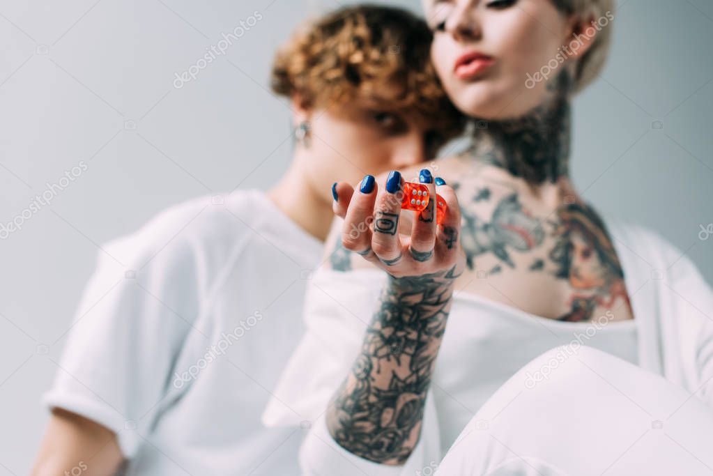 selective focus of tattooed girl holding red dice near boyfriend isolated on grey
