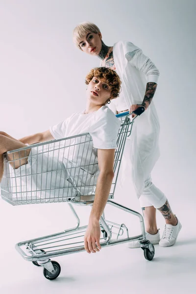 Attractive Blonde Girlfriend Pushing Shopping Cart Boyfriend Isolated Grey — Stock Photo, Image