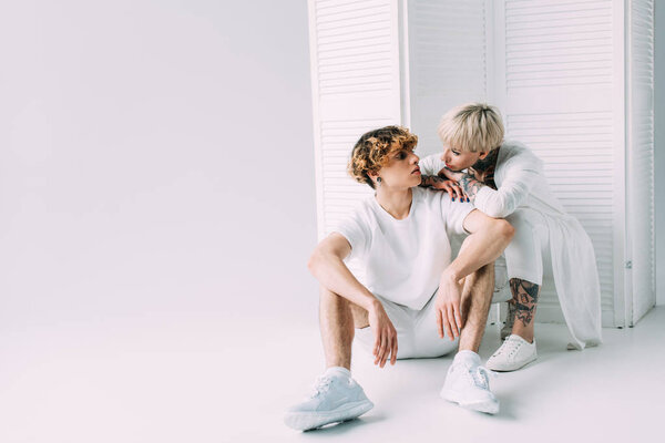 attractive girl and handsome man looking at each other and sitting on grey background