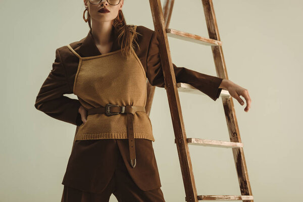 cropped view of fashionable woman in vintage style posing near wooden ladder isolated on beige