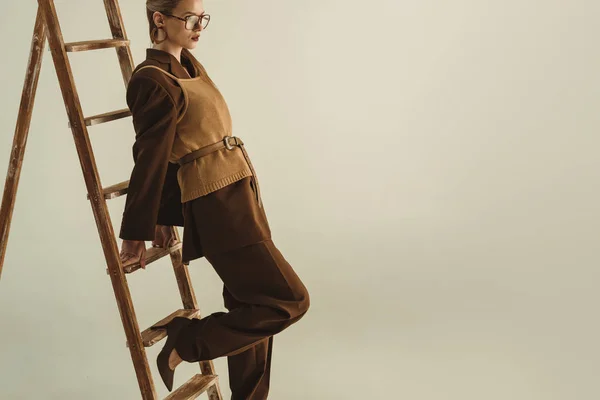 レトロなスタイルでベージュに分離された木製のはしご近くポーズ美しいモデル — ストック写真