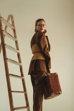 merdiven üzerinde bej izole yakınındaki vintage seyahat çantası ile poz güzel şık kız 