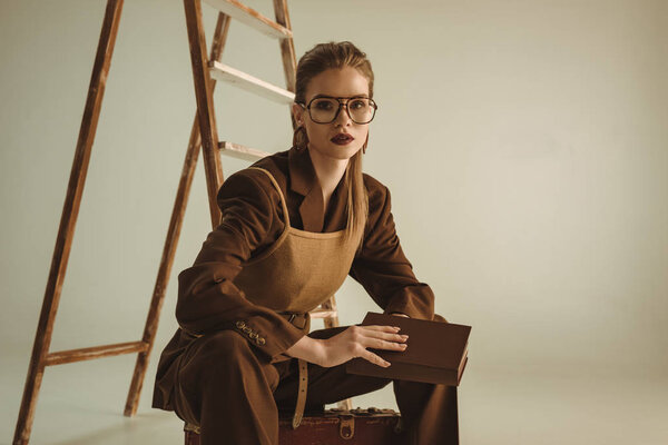 attractive girl holding book and sitting near ladder on beige