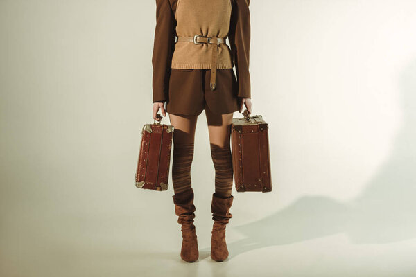 cropped view of young woman holding vintage travel bags on beige