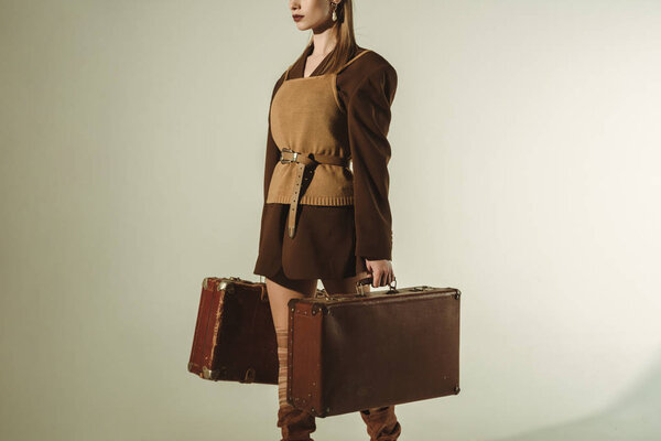 cropped view of stylish woman holding retro travel bags on beige