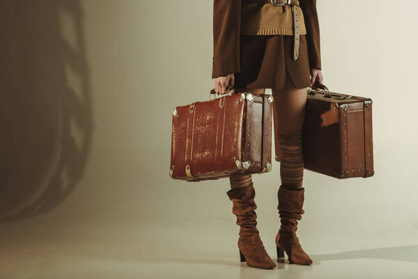 частичный вид модной женщины, держащей винтажные чемоданы на бежевом

