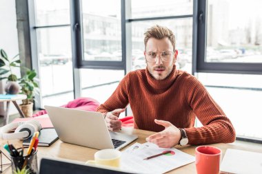 bilgisayar masasında oturan, kameraya bakıyor ve loft Office belge üzerinde çalışan yakışıklı rahat iş adamı