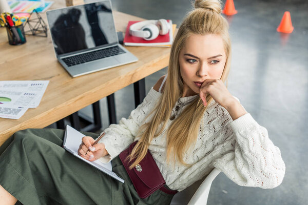 beautiful pensive female it specialist sitting with notebook at comtuter desk in loft office