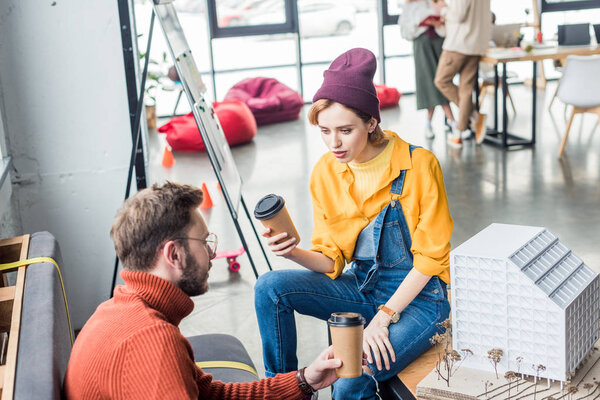 focused female and male architects with coffee to go working on house model in loft office