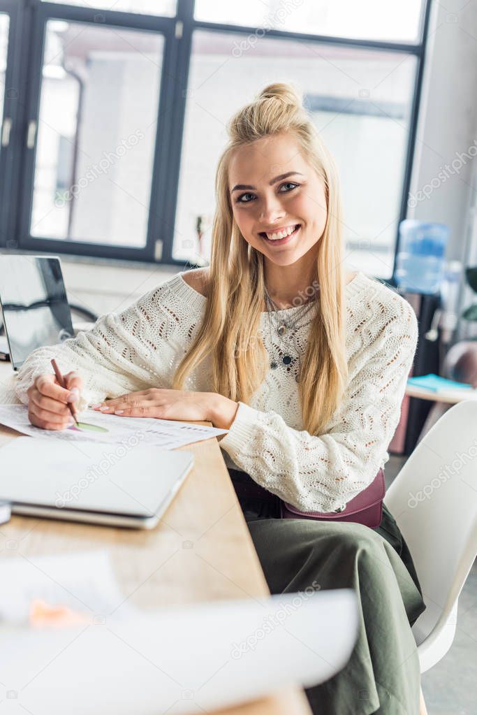 beautiful female architect looking at camera  and working on blueprint in loft office