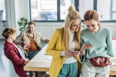 güzel arka plan meslektaşları ile çatı ofiste akıllı telefonlar kullanarak rahat iş kadınları gülümseyen