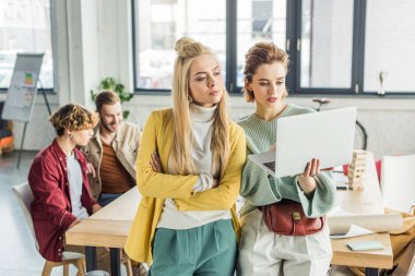 dizüstü bilgisayar kullanarak ve arka plan erkek meslektaşları ile çatı Office başlangıç proje üzerinde güzel odaklı rahat iş kadınları